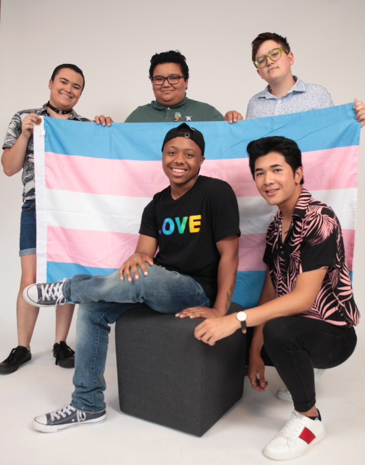 Five trans youth smile around a trans flag