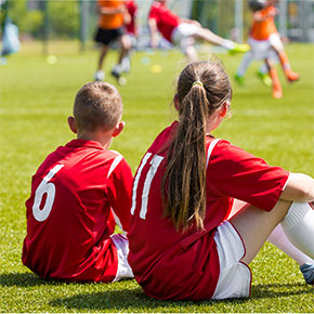 Two soccer players sitting on the grass with their backs to the camera