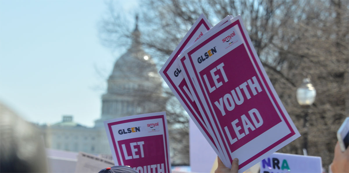 A protestor at the Washington, D.C. March for Our Lives demonstration holds up a GLSEN sign that reads: Let Youth Lead. The United States Capital Building stands in the near distance. 