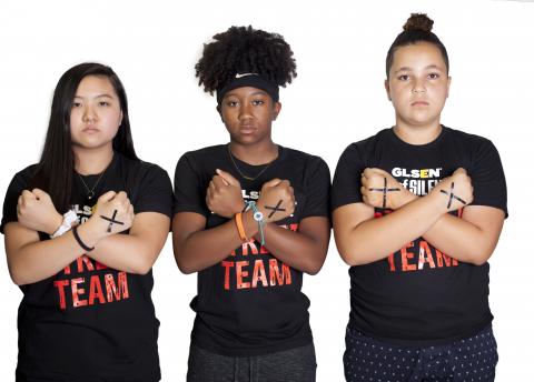 Three National Student Council members, all members of GLSEN's Day of Silence Street Team, stand in a row and hold their arms up to their chest in an X. On the backs of their hands are X's in black tape.
