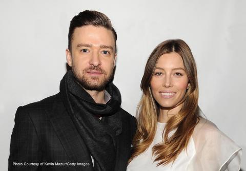 Justin Timberlake, left, dressed in a black plaid sport coat, and Jessica Biel, right, dressed in a white blouse, smile into the camera against a white backdrop.