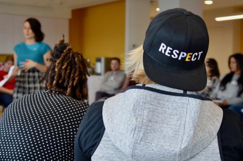 Student is facing a speaker with their back turned to the camera. The student is wearing a GLSEN Respect hat backwards.